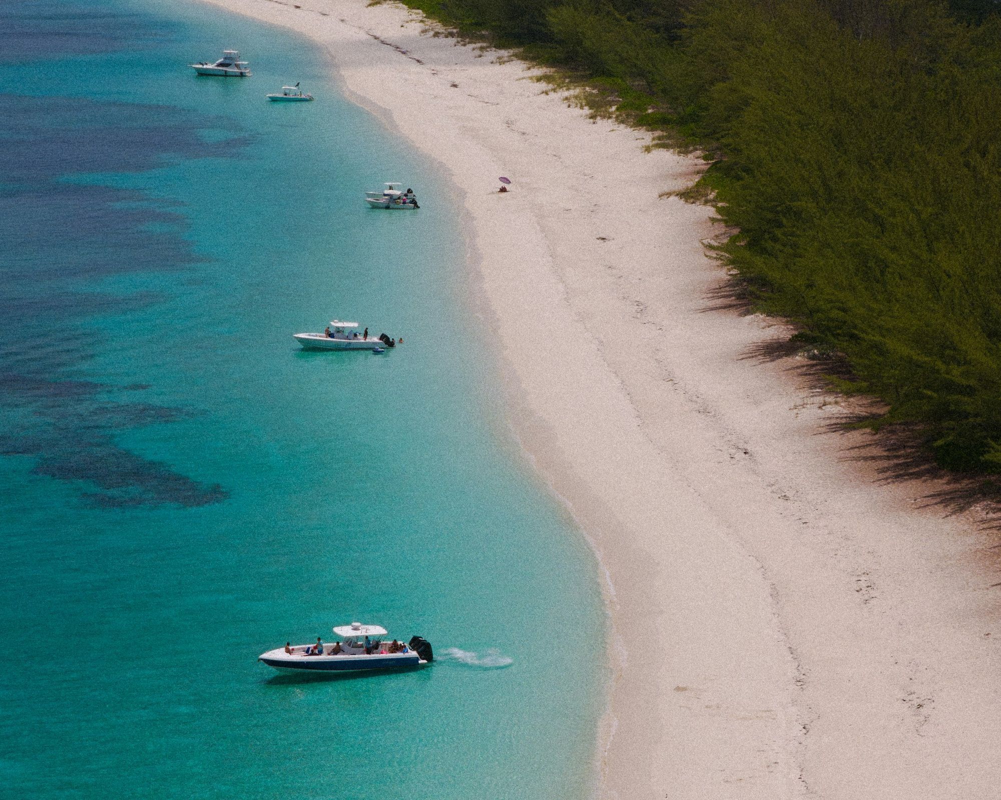 Aerial view of a white-sand beach and turquoise water with small boats near Nassau, The Bahamas